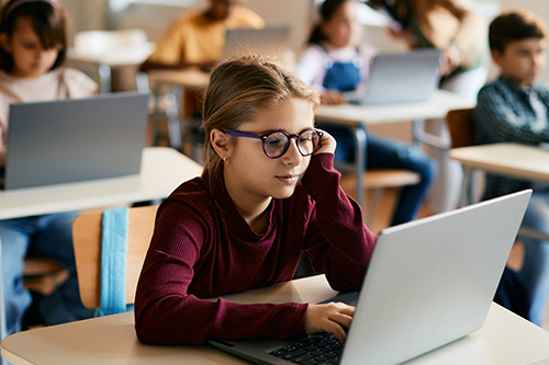 blondes maedchen mit brille lernt an einem laptop in der mittelstufe